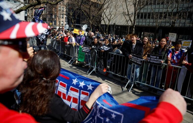 Two crowds shouting at each other. They are standing several metres apart. Metal barriers are keeping the Trump supporters and Trump opponents apart.