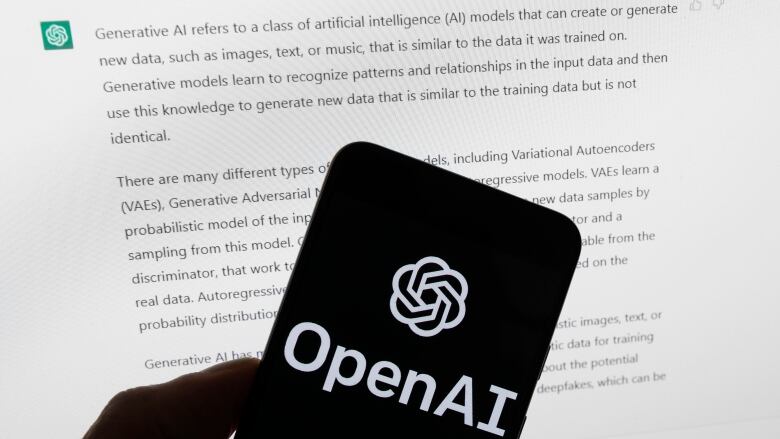 The OpenAI logo is seen on a mobile phone in front of a computer screen displaying output from ChatGPT, on March 21, 2023.