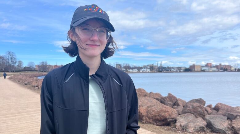 A woman stands on a boardwalk in front of water on a sunny day. 