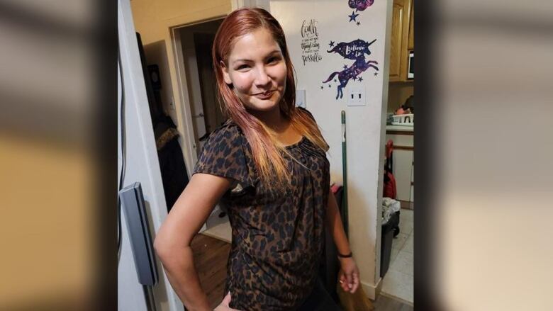 A woman in a leopard-print shirt with reddish shoulder-length hair stands in a doorway.