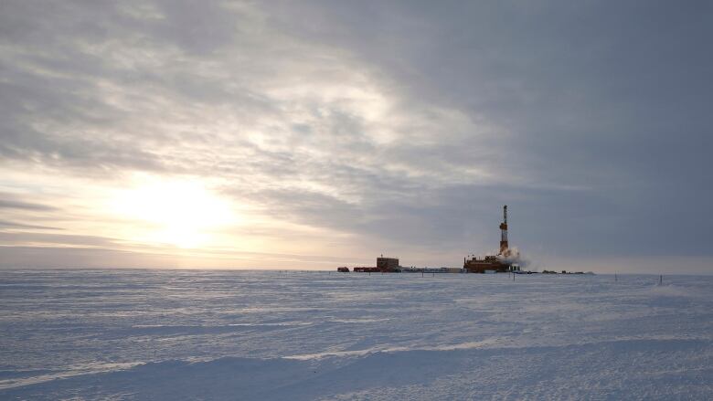 A large oil drilling rig is seen from a distance on a snowy expanse.