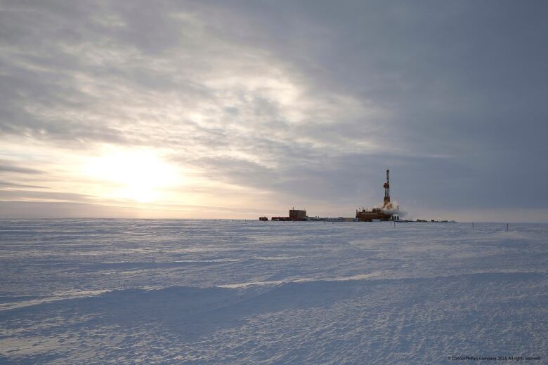 A large oil drilling rig is seen from a distance on a snowy expanse.