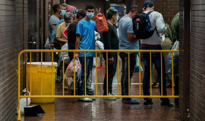 A group of people line up behind a fence inside a bus terminal with their luggage.