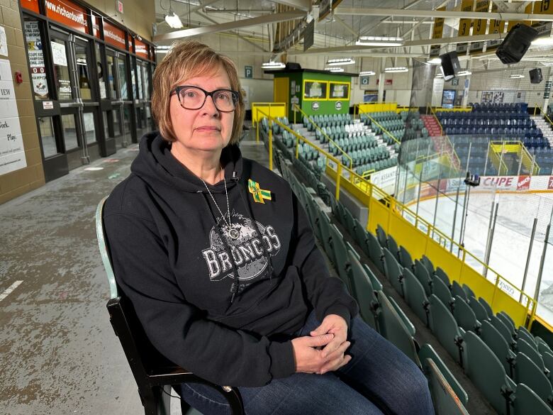 A woman with glasses sits in a hockey arena with a somber look on her face.