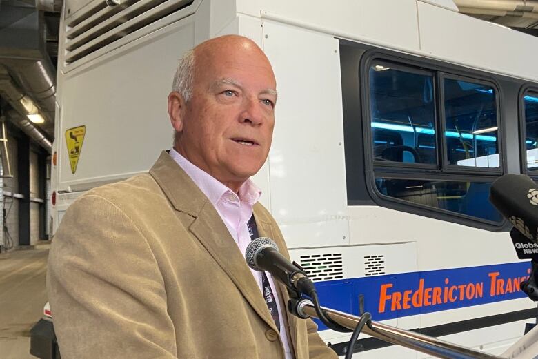 A man speaks while standing at a podium with a transit bus in the background.