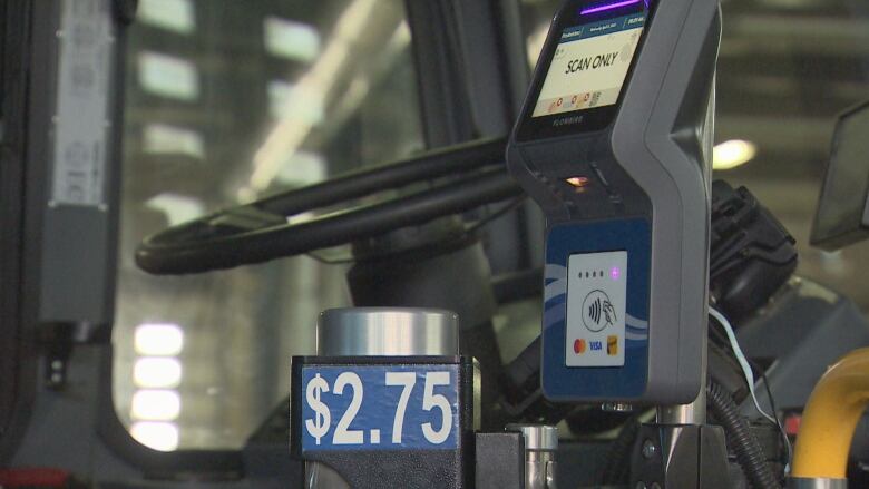 The inside of a transit bus shows an electronic device for paying the fare, and a sticker showing the fare price.