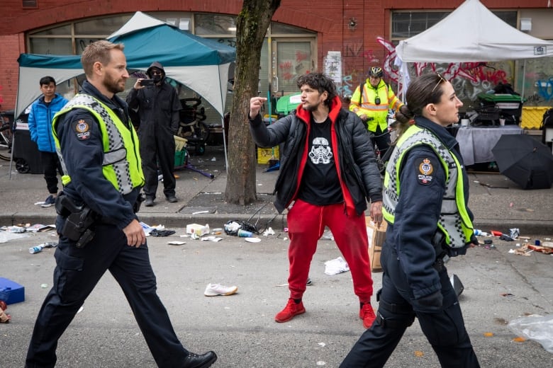 A man wearing red sweatpants yells as two police officers walk past