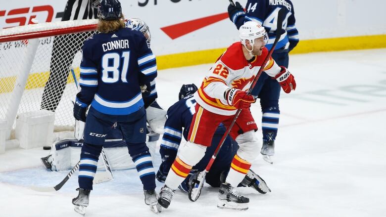 A Calgary Flames player skates away from the Winnipeg net, his stick raised in celebration, while three Winnipeg Jets look away in dejection.