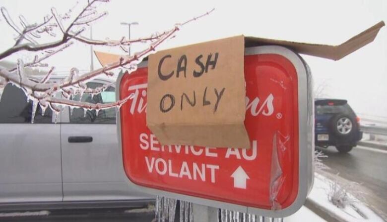 A sign that says cash only hangs on a drive-thru sign covered in ice.