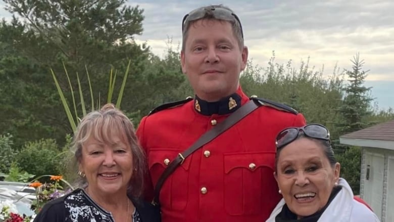 A man in RCMP uniform stands with two older/elderly women on each side. 