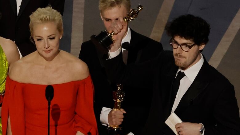 People stand on a stage, holding aloft the Academy Awards they have just won.