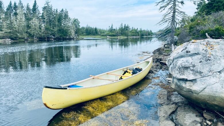 Canoe is shown in the water near a rocky water's edge. 