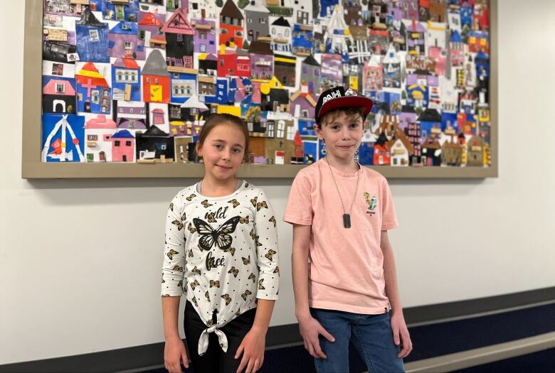 Two young children stand in front of a mural.