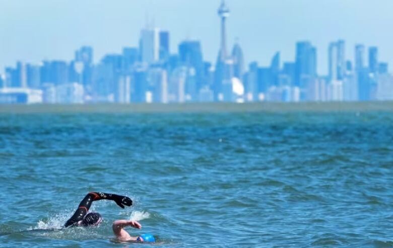 Two people swim, with a city skyline in the background.