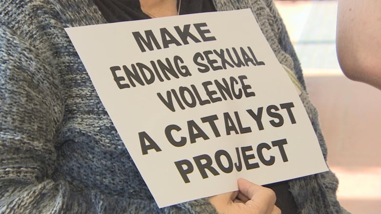 Woman holding a sign that says make ending sexual violence a catalyst project