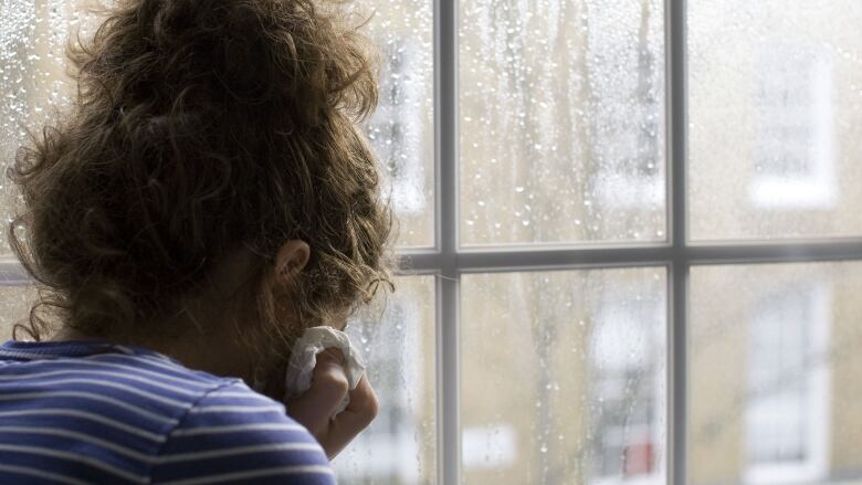 A woman sits by a window with rain drops on it.