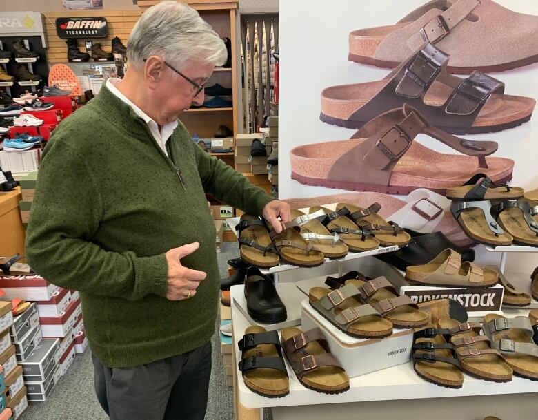 Old man inside shoestore touching one of the display shoes.