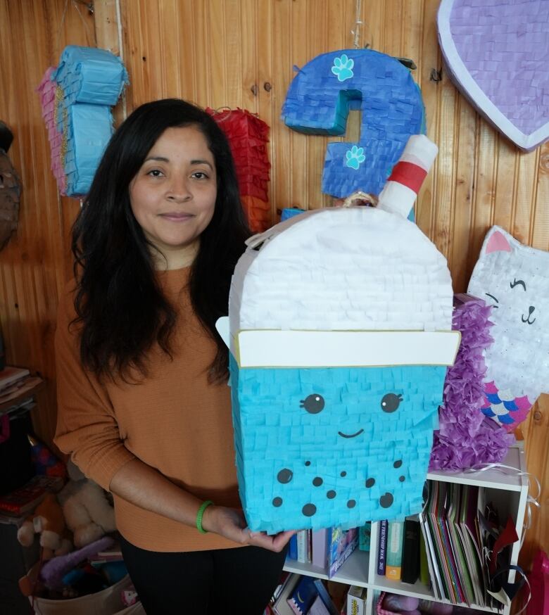 A woman with long brown hair hold up a blue and white pinata that looks like a smiling glass of bubble tea.