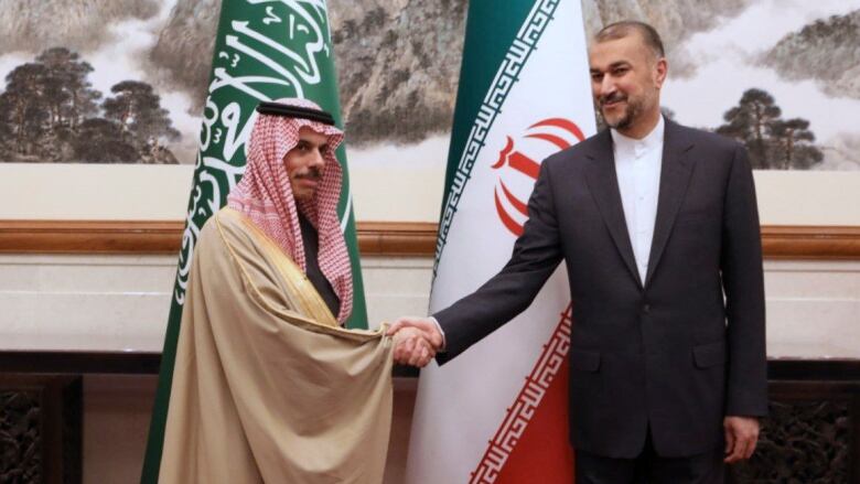 Two diplomatic officials  one from Saudi Arabia and the other from Iran  pose for a photo while shaking hands.