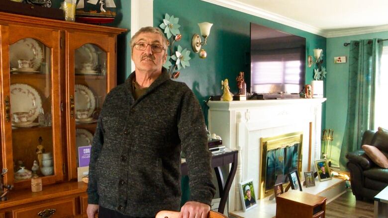 A mean with glasses and a grey sweater stands near a table in a dining room.