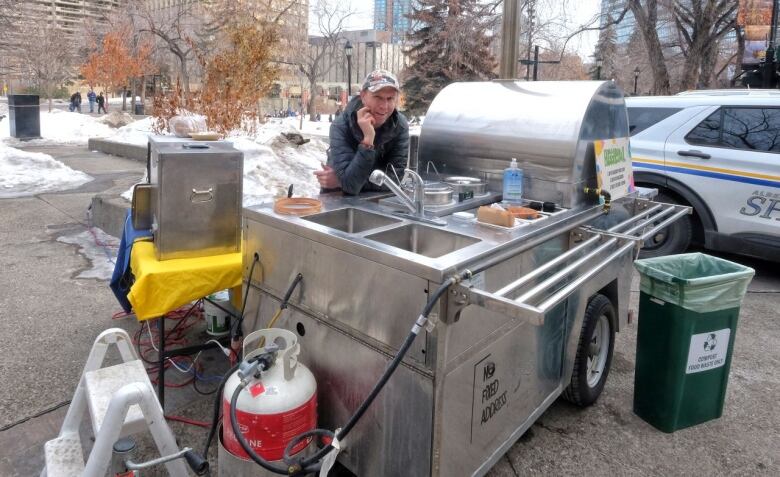 A man leans up against a food cart.