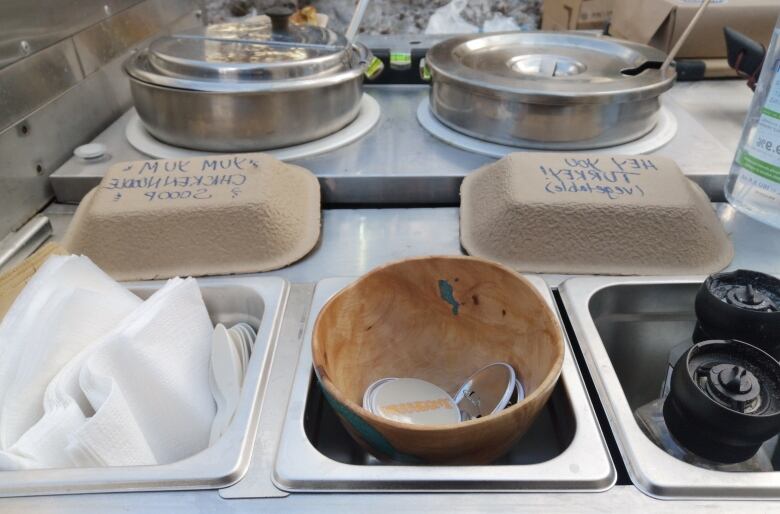 Bowls of pins and containers of soup in a cart.