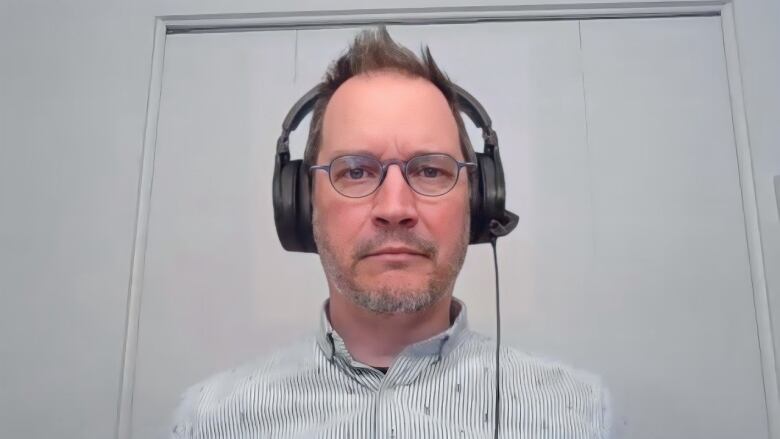 A man with glasses and a striped shirt looks at the camera while wearing large black headphones