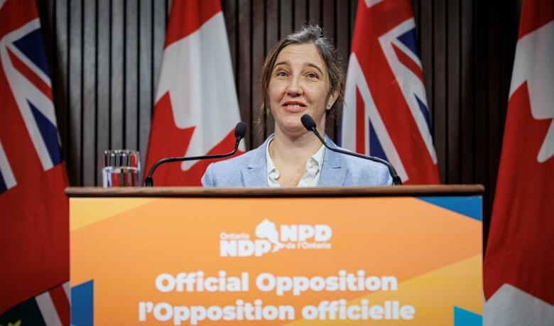 Jessica Bell stands behind an orange placard saying 'NDP, Official Opposition.'