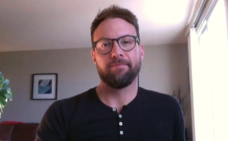 A white man with glasses sits in a living room.