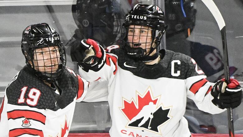 A Canadian female hockey player points her finger as she is embraced by a teammate.