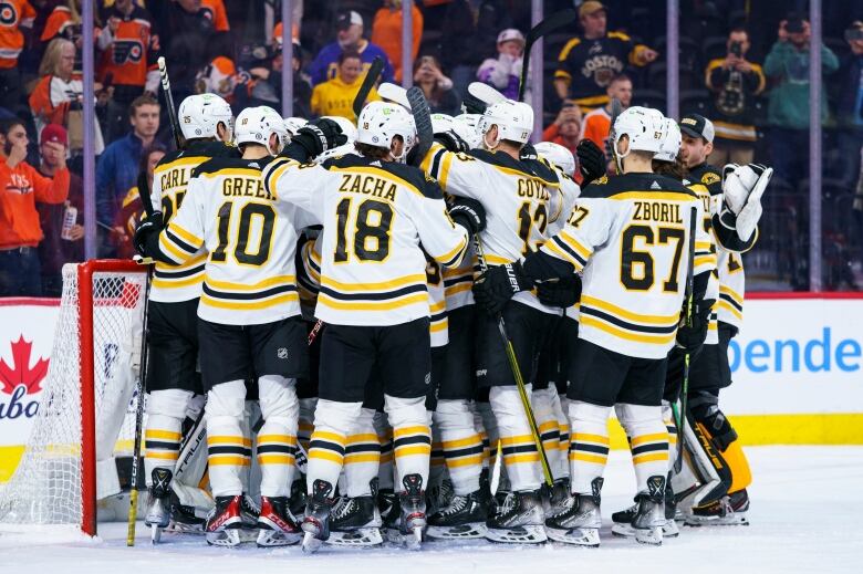 A large group of hockey players in black, white and gold uniforms gather tightly near the net with their backs to the camera. Fully visible uniforms say 