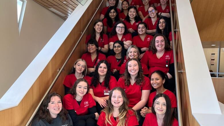 A group of students in red t-shirts sits on a staircase. 