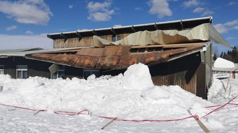 Snow is piled in front of a two-storey building. The overhang of the lower level is collapsed and leaning forward.