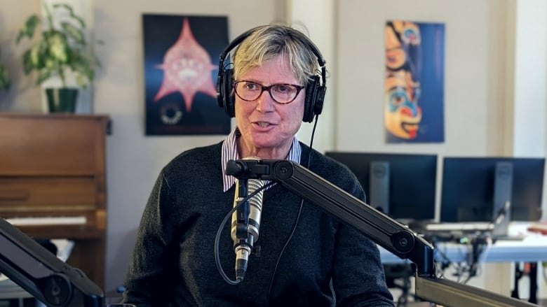 A woman with glasses speaks into a microphone during an interview in a radio studio.