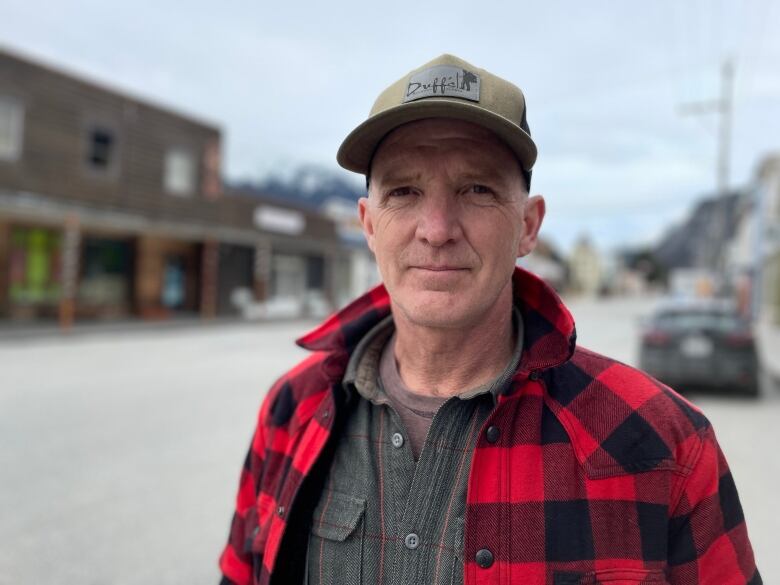 A portrait of a man in a cap and red plaid coat outside.