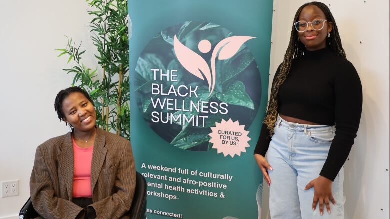 Two women smiling in front of a sign that reads 