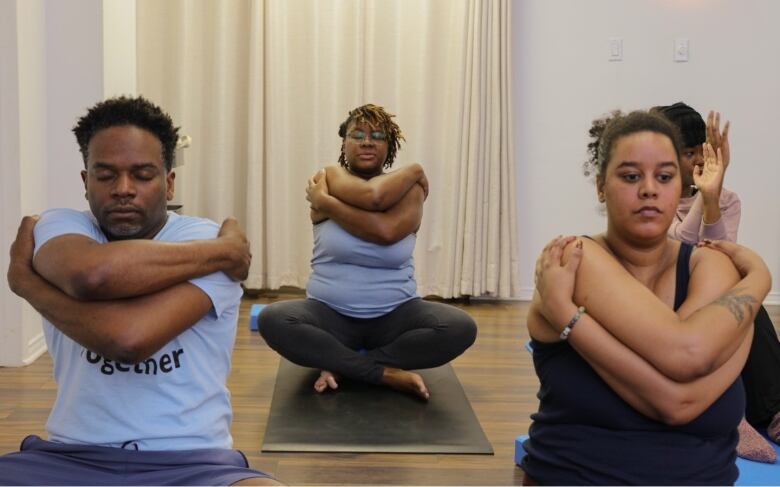 People sitting on mats striking yoga poses in a studio. 