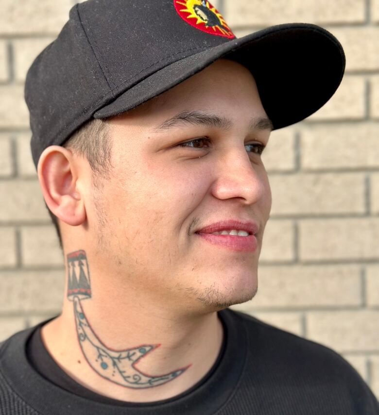 Profile of man wearing ball cap with neck tattoo of antler rattle.