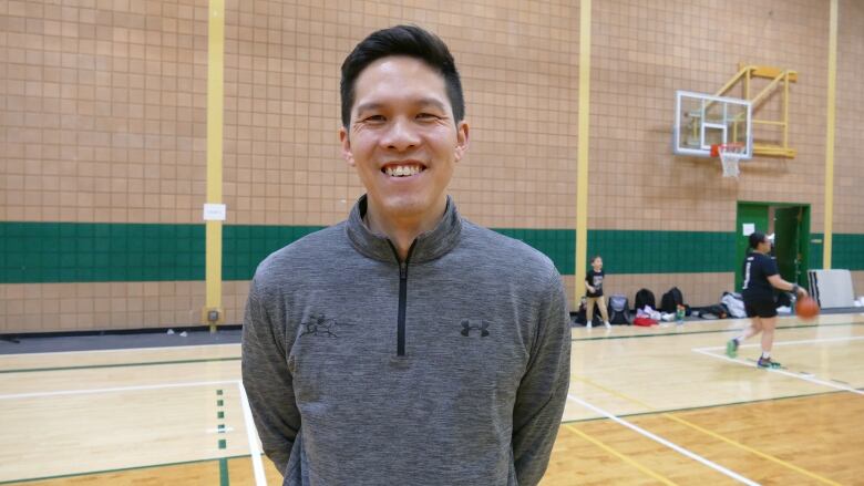 Coach Eric Sung stands with his hands behind his back, smiling at the camera. 