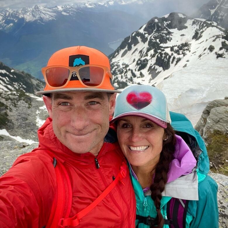 A man and a woman smile for the camera, with snow-covered mountains in the background.