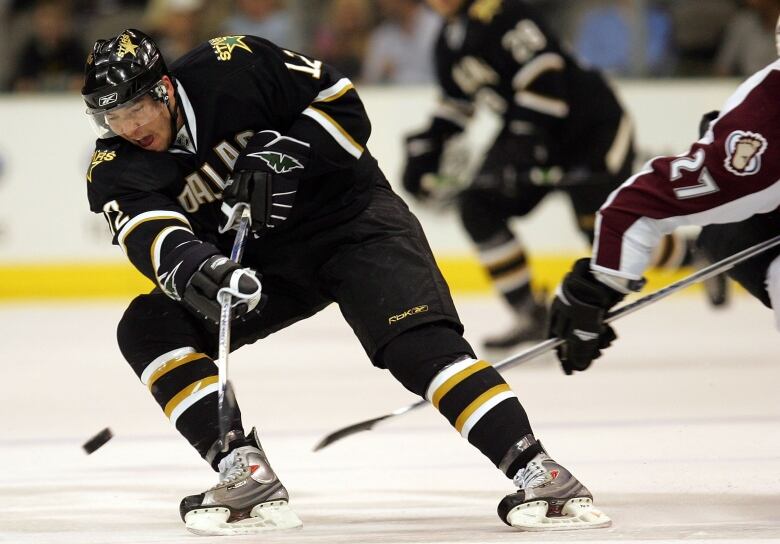 An NHL hockey player in a Dallas Stars uniform grimaces with effort as he chases the puck. 