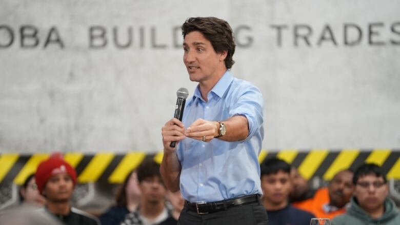 A man in a blue shirt and short dark hair speaks to a crowd.