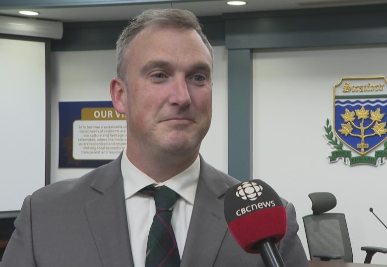 Stratford Councilor Jeff MacDonald stand at the CBC mic for an interview in a light color suit and tie. 