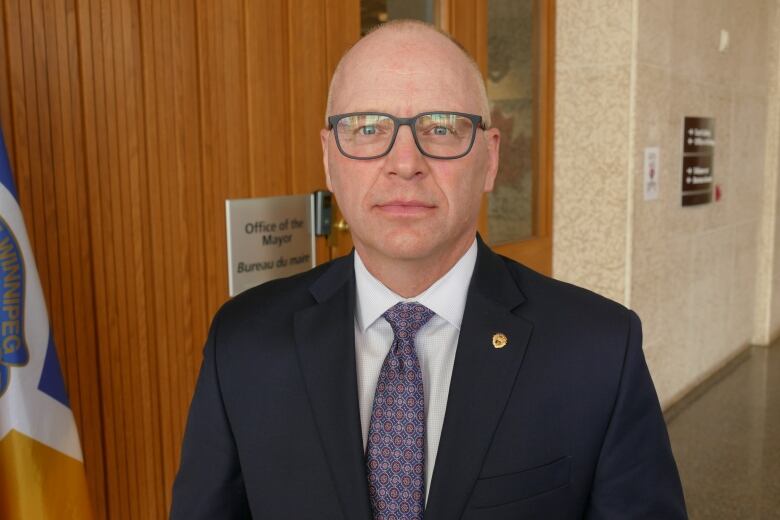 A man in a dark blazer and purple patterned tie and white shirt looks ahead.