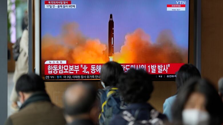 A TV screen showing a missile is watched by a gathered crowd