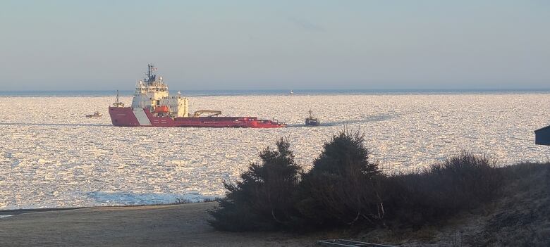 A red and white ice-breaking ship makes its way through the ice as a fishing boat follows in its trail.