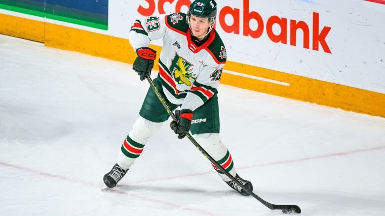 A player in a white, orange and black jersey handles the hockey puck during a game.