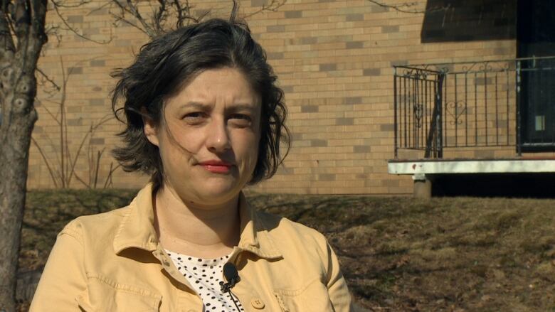 A woman stands in front of an apartment building. 