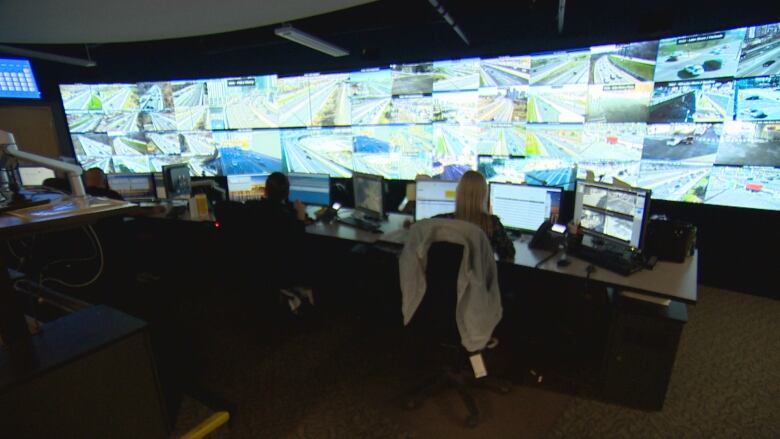 People sit at desks infront of multiple screens showing traffic.