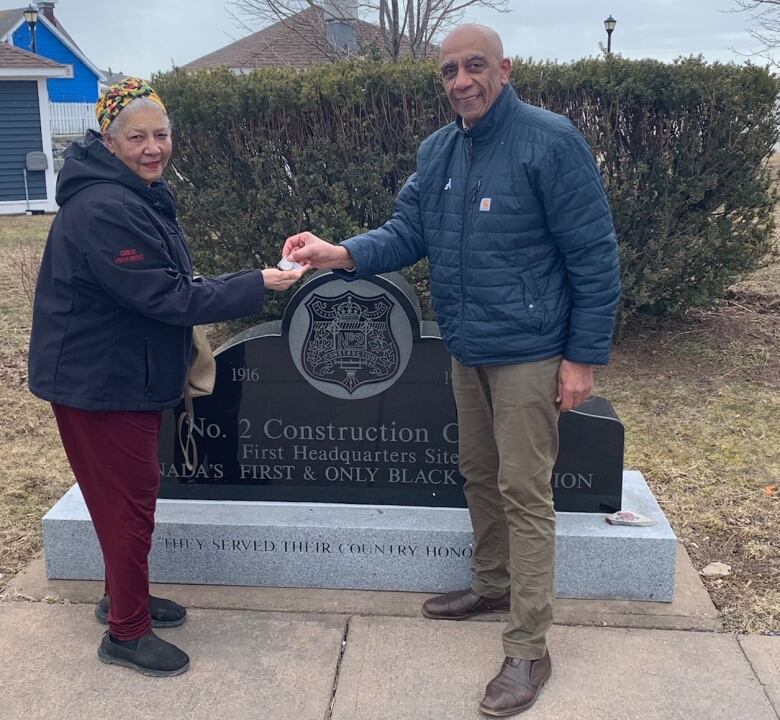 A man and woman hold a medal standing in front of a monument for the No. 2 Construction Battalion.